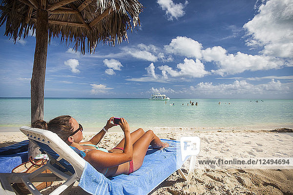 Eine junge Frau macht ein Foto mit ihrem Smartphone  während sie sich während eines Urlaubs in Cayo Coco  Kuba  am Strand entspannt.