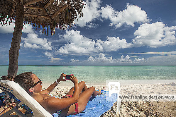 Eine junge Frau macht ein Foto mit ihrem Smartphone  während sie am Strand von Cayo Coco  Kuba  entspannt.