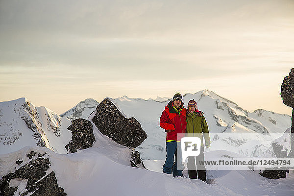 Ein junges Paar posiert für ein Foto auf dem Gipfel eines Berges im letzten Licht des Tages während einer Skitour in den Coast Mountains bei Whistler  British Columbia  Kanada.