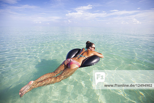 Eine junge Frau schwimmt auf einem aufblasbaren Wasserspielzeug im flachen türkisfarbenen Wasser während ihres Urlaubs in Cayo Coco  Kuba.