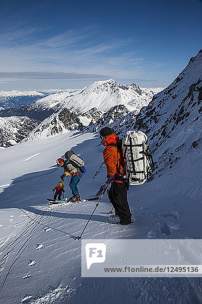 Skifahrer fahren während der Spearhead Traverse in den Coast Mountains von British Columbia  Kanada  eine steile Kerbe zwischen zwei Bergen hinauf.