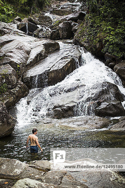 A Young Man Swimming In A Pool At The Base Of A Waterfall In Puerto Rico
