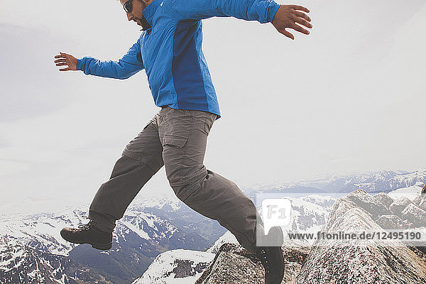 Ein Wanderer springt zwischen zwei Felsen auf dem Gipfel des Needle Peak  BC  Kanada.