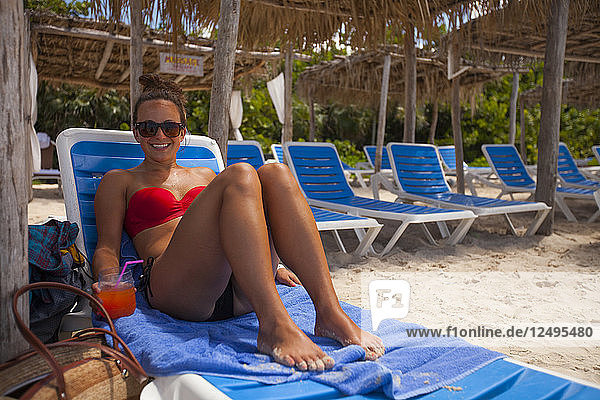 A young woman wearing a bikini and holding a drink relaxes at the beach while on vacation in Cayo Coco  Cuba.