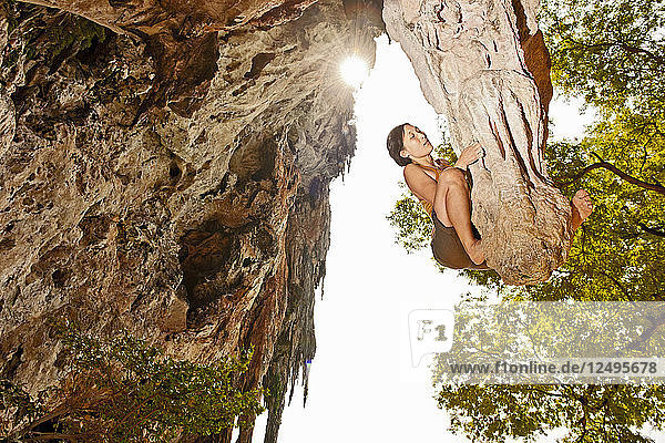 Frau beim Bouldern auf einem Kalkstein-Stalagtit am Strand von Railay in Thailand
