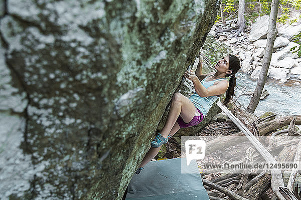 Weibliche Athletin klettert auf einem Felsblock draußen am Fluss in Maryland