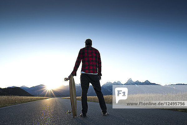 A skateboarder pauses to watch the sun set over the Grand Teton Mountains in Jackson Hole  Wyoming.