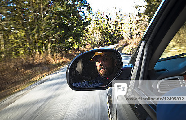 Das Gesicht eines Mannes spiegelt sich im Rückspiegel eines Lastwagens  während er eine Straße in Squamish  British Columbia  entlangfährt.