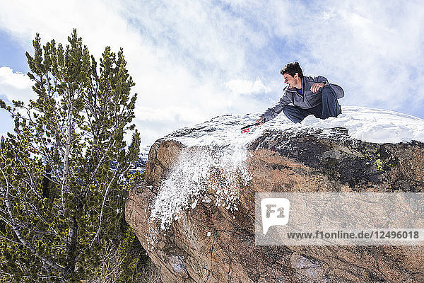 Männlicher Kletterer reinigt die Spitze eines Felsblocks vom Schnee  bevor er im Rocky Mountain National Park  Colorado  klettert.
