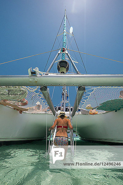 Eine junge Frau geht nach dem Schwimmen in tropischen Gewässern in der Nähe von Kuba eine Falltreppe hinauf  die zu einem Katamaranboot führt.
