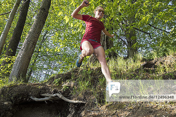 Female Runner Jumping Across A Drop Along The Trail