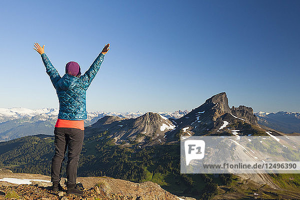 Eine junge Frau jubelt  nachdem sie den Gipfel des Panorama Ridge im Garibaldi Provincial Park  British Columbia  Kanada  erreicht hat. Der Black Tusk Mountain ist der markante Gipfel am Horizont.