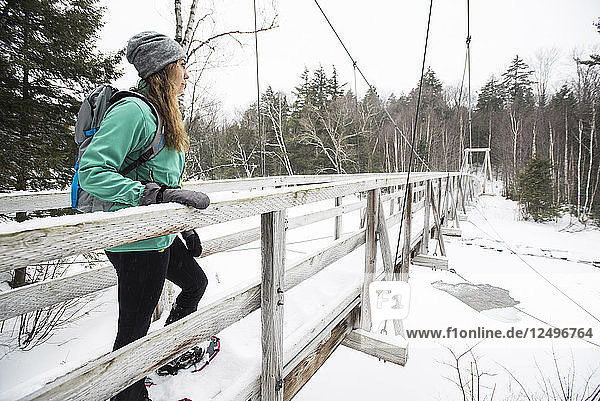 Eine Wanderin macht auf einer Brücke im Winter eine Pause