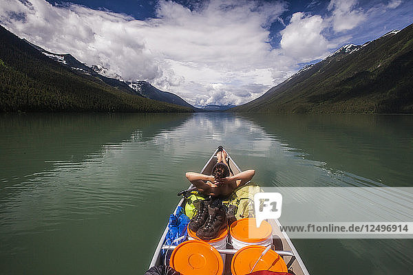 Ein junger Mann entspannt sich im vorderen Teil eines Kanus  während er während einer mehrtägigen Kanutour durch den Bowron Lake Provincial Park  British Columbia  Kanada  über den Lanezi Lake paddelt.