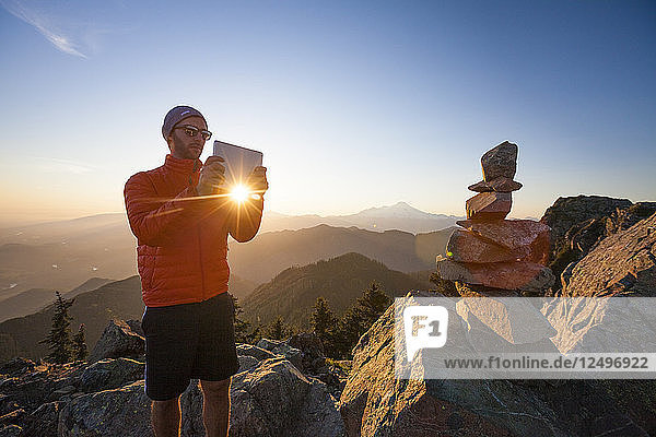 Ein Wanderer fotografiert mit einem Tablet einen Steinhaufen auf dem Gipfel des Sauk Mountain  Washington.