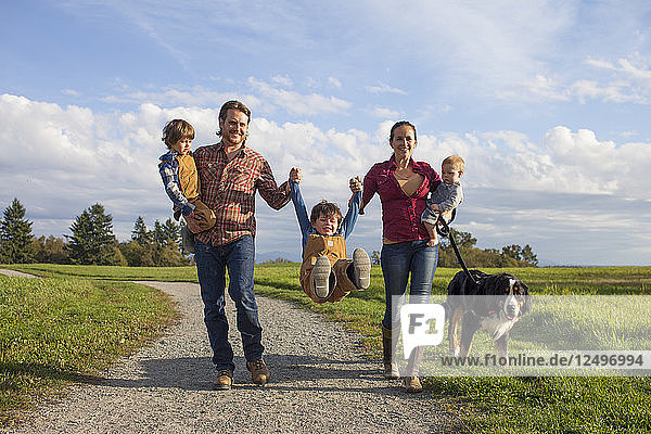 Eine fünfköpfige Familie mit Hund spaziert spielerisch über einen Kiesweg in einem örtlichen Park in der Nähe von Vancouver  Kanada.