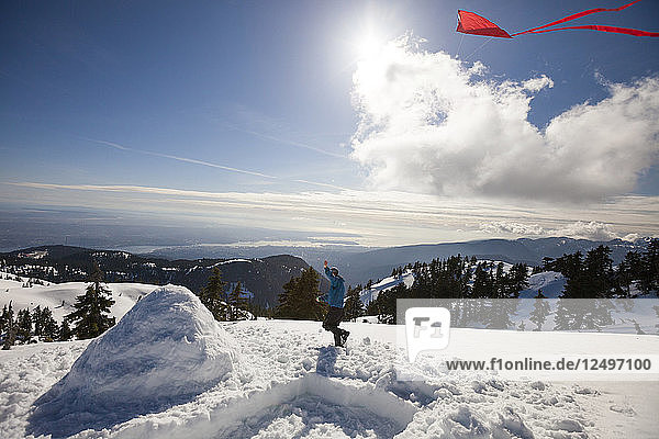 Ein Wanderer  der einen Drachen auf dem Gipfel eines schneebedeckten Berges fliegt  während er neben seinem Iglu läuft