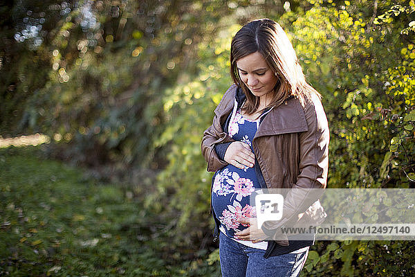 Outdoor portrait of a beautiful young pregnant woman holding her baby bump.