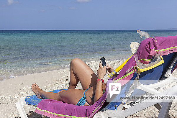 Mädchen mit Smartphone beim Entspannen auf Liegestuhl am Strand in Kuba