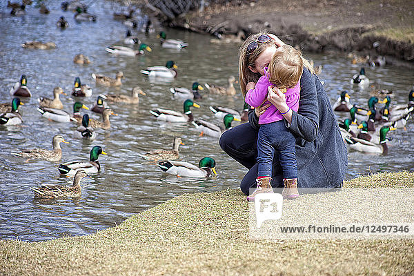 Kleinkind und Mutter füttern Enten im Park.