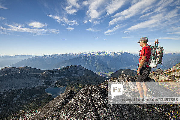A backpacker looks down at Valentine Lake from a rocky ridge near Saxifrage Mountain  Pemberton  British Columbia  Canada.
