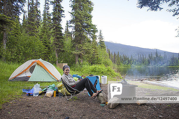 A woman relaxes at a lakeside campsite in Bowron Lake Provincial Park  British Columbia  Canada.