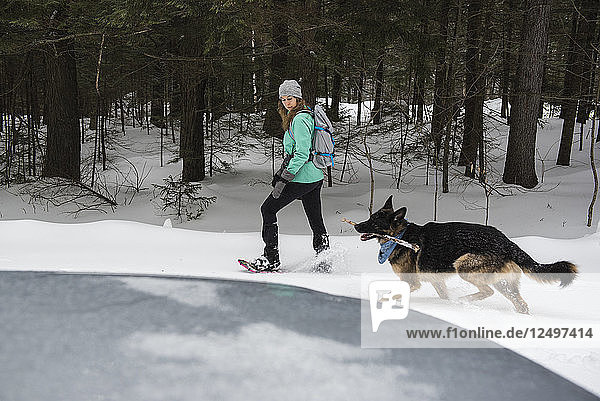 Frau und Hund beim Schneeschuhwandern im Wald.