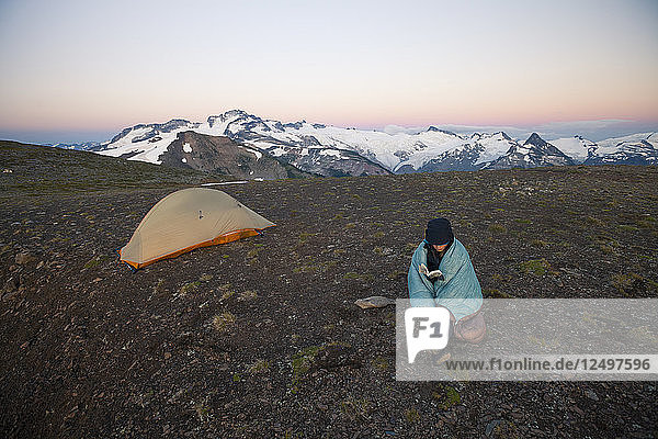 Eine junge Frau liest ein Buch beim Zelten auf der Panorama Ridge im Garibaldi Provincial Park  British Columbia  Kanada.