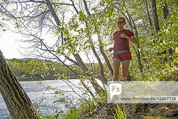 Weibliche Läuferin läuft auf einem Pfad am Ufer des Flusses