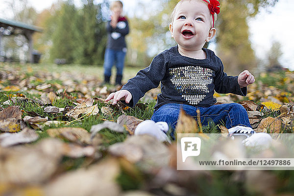 A Smiling Baby Playing With Leaves At Park