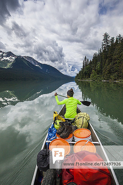 A young woman paddling across Lanezi Lake during a multi-day canoe trip through Bowron Lake Provincial Park  British Columbia  Canada.