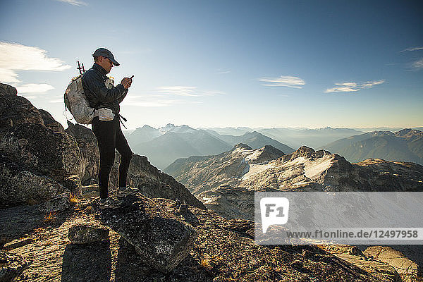 An ultralight backpacker sends a safety message from his smartphone while hiking high in the mountains near Whistler  BC  Canada.