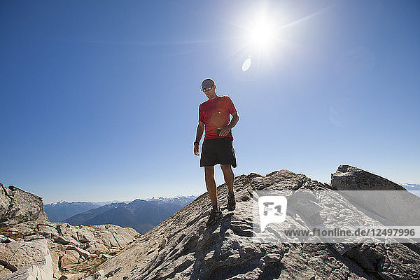 A hiker walks along a rocky ridge while holding a smartphone on the summit of Cassiope Peak near Pemberton  British Columbia  Canada.