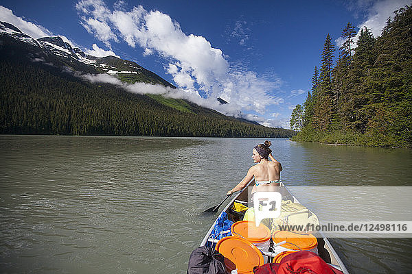 A young woman canoeing across Lanezi Lake during a multi-day canoe trip through Bowron Lake Provincial Park.