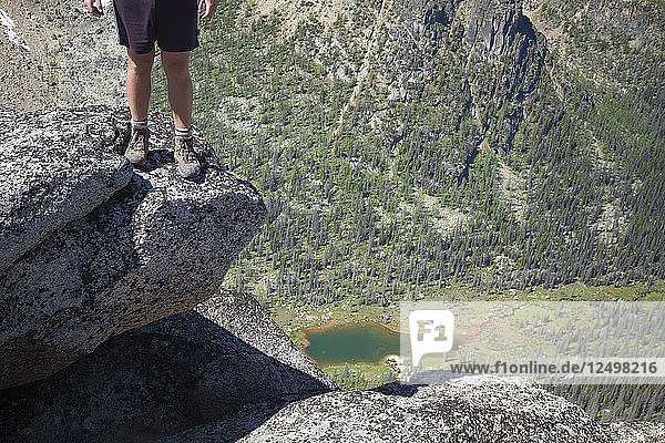A hiker stands on the edge of a granite boulder high above the valley below in Cathedral Lakes Provincial Park  British Columbia  Canada.