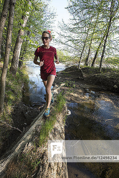 Weibliche Trailrunnerin balanciert auf einem langen alten Baumstamm