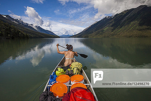 A young woman canoeing across Lanezi Lake during a multi-day canoe trip through Bowron Lake Provincial Park  British Columbia  Canada.