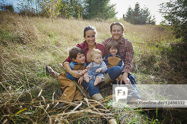 Ein lustiges Porträt einer lebhaften fünfköpfigen Familie  die auf einem Feld sitzt.