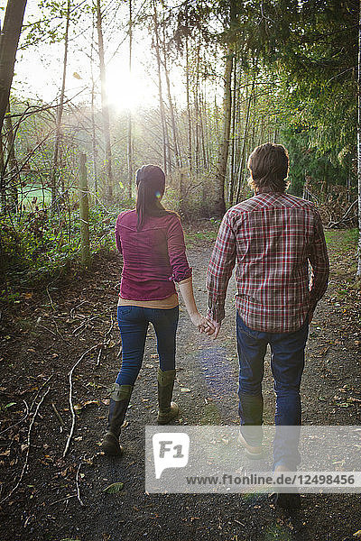 Ein junges Paar hält sich an den Händen  während es in einem örtlichen Park spazieren geht.