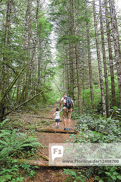 Young Child With Her Dad Hiking Through The Forest On A Trail In Oregon