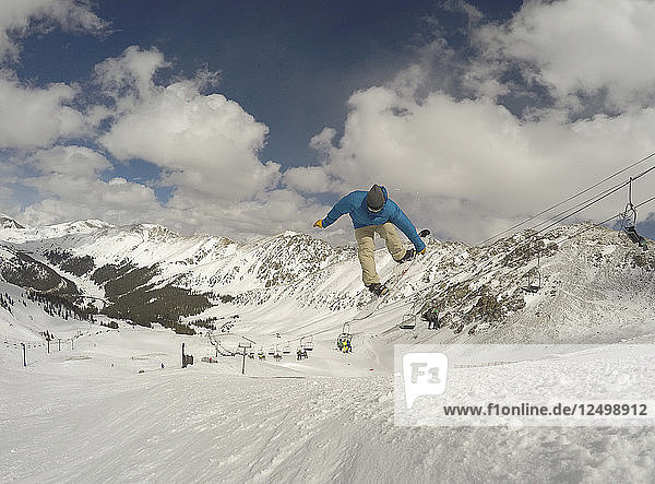 Mann springt und packt sein Snowboard gekonnt im Arapahoe Basin Ski Area