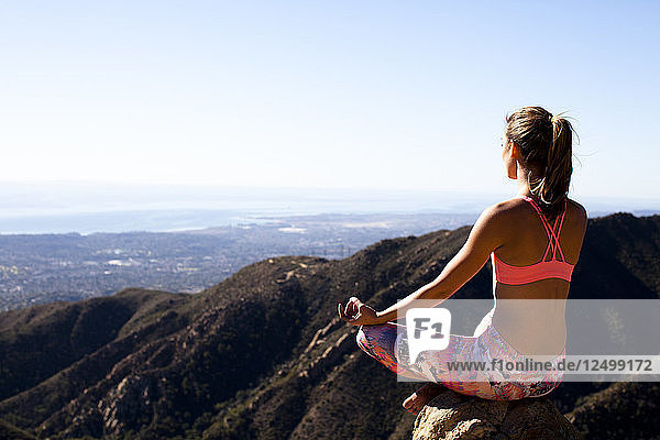 Eine Frau in bunten Hosen sitzt mit gekreuzten Beinen auf dem Lower Gibraltar Rock in Santa Barbara  Kalifornien. Der Lower Gibraltar Rock bietet eine großartige Aussicht auf Santa Barbara und den Pazifischen Ozean.