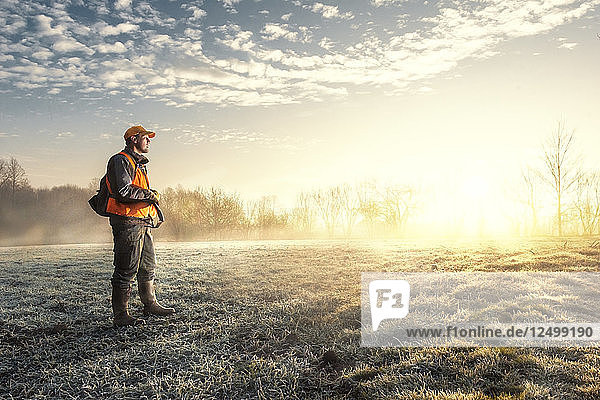 Jäger blickt über die sonnenbeschienene Wiese am frostigen Morgen  in der Nähe von Kraljevo  Serbien. Aufgenommen bei der Jagd auf Fasane.