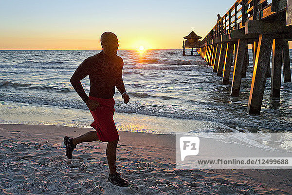 Man running on the beach at sunset with a pier in the background