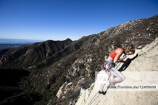 A woman wearing a red tank top and striped pants pulls up rope while climbing The Rapture (5.8) on Lower Gibraltar Rock in Santa Barbara  California. The Rapture is a very nice and unbelievably well protected route on the left ar?™te of Lower Gibraltar Rock.