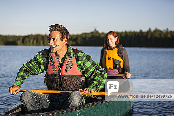 Ein junges Paar paddelt ein Kanu durch Morgennebel auf Long Pond in der Nähe von Greenville  Maine