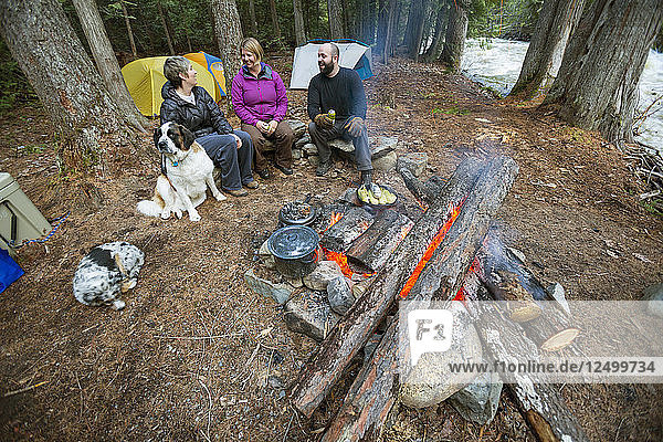 Drei Camper sitzen am Lagerfeuer und warten auf ihre Mahlzeit
