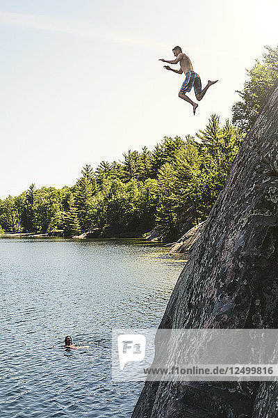 Ein junger Mann springt von einer Klippe in den George-See  während eine andere Person von unten schaut