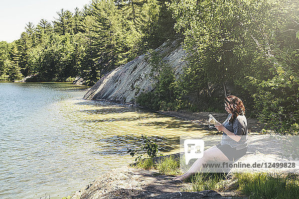 Eine junge Frau liest in aller Ruhe am Ufer des George Lake an einem hellen Sommertag