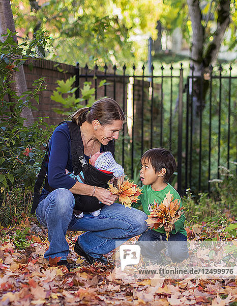 Mutter mit Baby spielt mit kleinen Jungen im Herbst Blätter